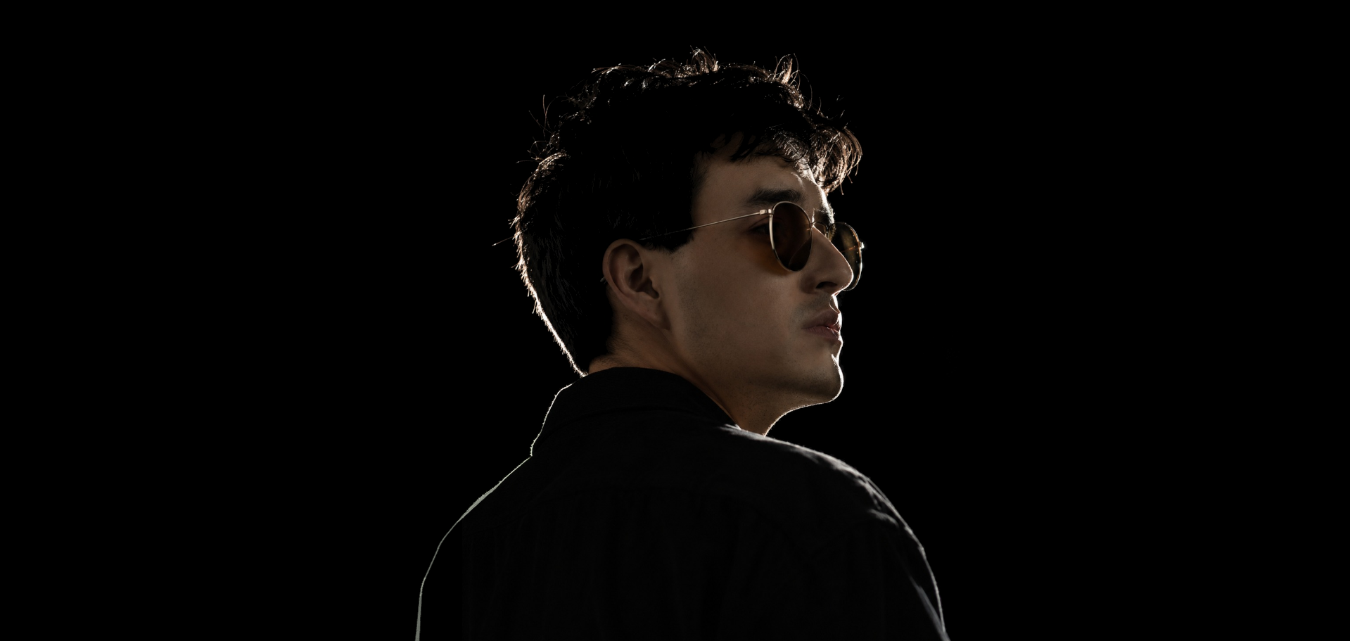 Portrait of Josué Gutiérrez looking over his shoulder, wearing round sunglasses